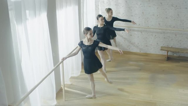 Three Young and Graceful Ballerinas Practicing at the Barre. Their Tutus are Black Tights White. Shot on a Sunny Day in a Modern Studio.  Shot on RED EPIC-W 8K Helium Cinema Camera.