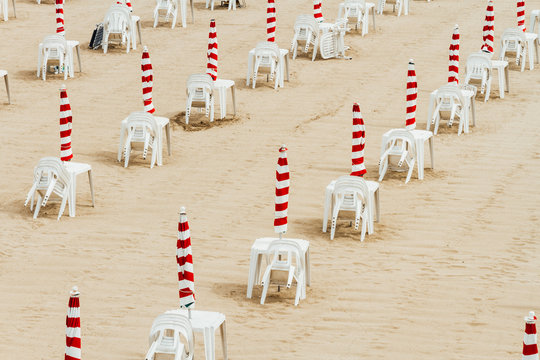 Several sunshades closed with plastic tables and chairs at a bea