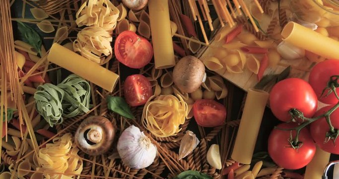 Dolly tilt down view of different variety of Italian pasta and ingredients