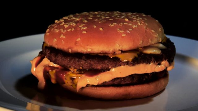 Burger on black background / Rotating hamburger  on a white dinner plate.
 Black background  
