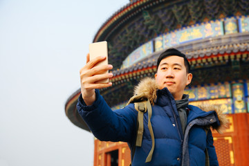 Asian man wearing winter jacket and using a smart phone over Chinese temple background (Selective focus)