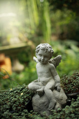 Cupid sculpture in garden, background for Valentine's day. Green color toned.