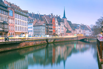 Picturesque quay and church of Saint Nicolas with mirror reflections in the river Ile during morning blue hour, Strasbourg, Alsace, France