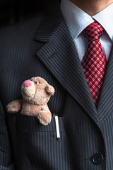 Close up with elegant stylish businessman keeping small teddy bear in his breast suit jacket pocket. Formal negotiations concept.