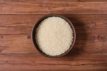 Raw rice in a clay plate on a wooden table old.