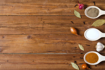 Wooden spoons with spices on a wooden table, space for text.