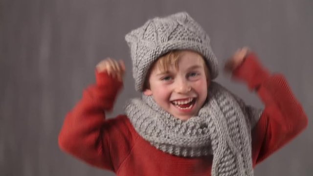 joyful beautiful child wearing winter clothes raising arms when snowing