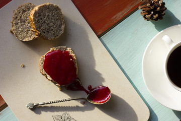 A hot morning coffee served in a beautiful cutlery with delicious brown bread on an orange and light cyan old wooden table.