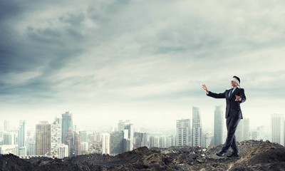 Young businessman in blindfold walking carefully and cityscape at background