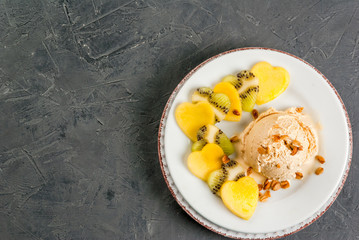 Romantic foods for Valentine's Day. Fruit salad with ice cream ball on a plate, top view. Fruits cut in the shape of hearts, copy space