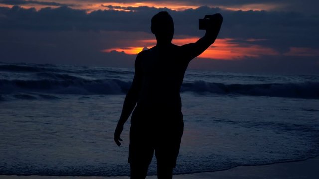Silhouette of man taking selfie photo with cellphone during sunset, super slow motion
