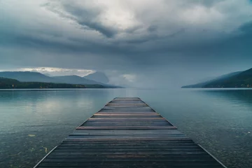 Fototapeten Dock mit Blick auf einen ruhigen bewölkten See. © RyanTangPhoto