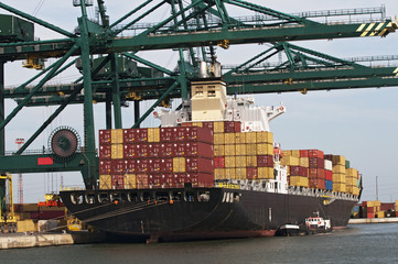 container ship at the dock in the harbor and be unloaded by large cranes.