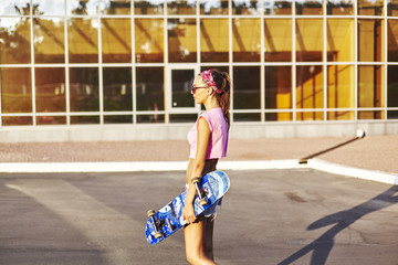 Beautiful hipster girl in a jeans shorts and pink shirt walking with skateboard near the green park, sexy style, adult, long legs, brunette, white shoes, sexy model, posing on camera