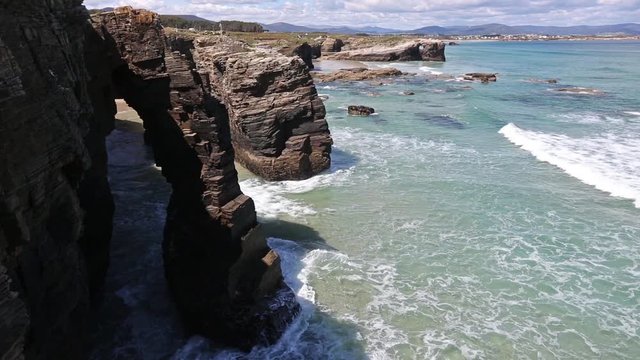 Natural rock arches and ocean surf on Cathedrals beach in low tide (Cantabric coast, Lugo, Galicia, Spain). View of the top. People are unrecognizable.
