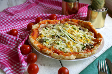 Homemade vegetarian pizza with lot of toppings: tomato sauce, mozzarella, zucchini, corn and champignons. Checkered napkin, cherry tomatoes and cacti laying around. Shallow depth of field.
