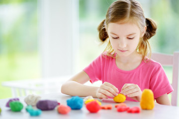 Cute little girl having fun with colorful modeling clay at a daycare