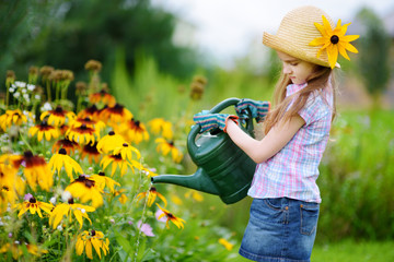 Cute little girl watering flowers in the garden