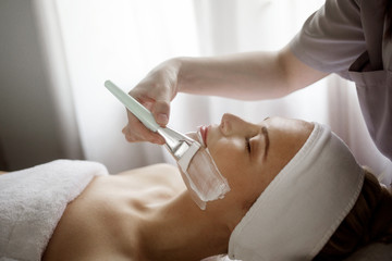 Midsection of therapist applying facial mask on woman in spa