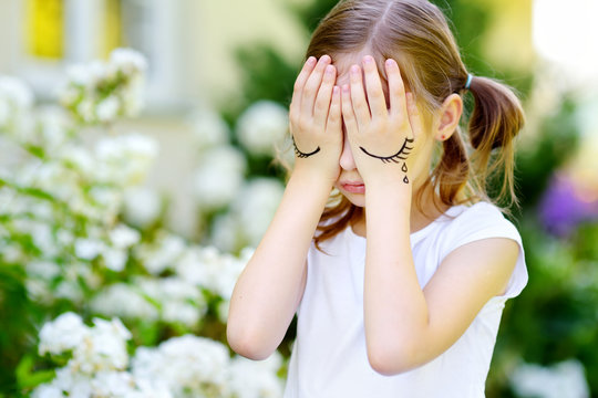 Cute little girl covering her face with her hands on summer day