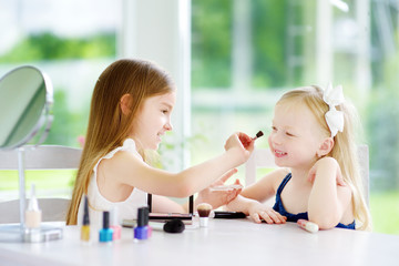 Two cute funny sisters applying make-up on sunny summer day at home