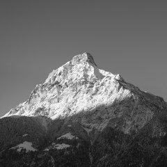 Switzerland, Alps. Sun rises and illuminates the tops of the mountains. Winter landscape, snow in the mountains. Moon is visible above the mountains. Black and White.