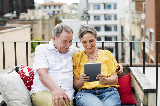 Cheerful senior couple using tablet computer while sitting on bench at terrace