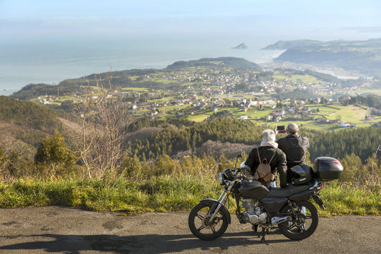 Senior couple photographing mountains while standing by motorcycle on road