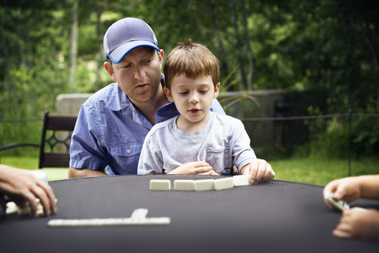 Father and son playing domino at table in backyard