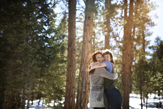 Cheerful friends hugging while standing in forest during winter