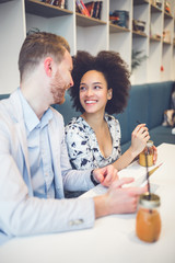 Happy middle age interracial couple sitting in cafe bar, smiling and looking at white tablet.