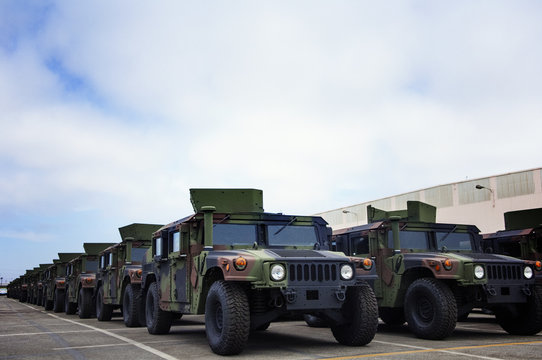 Military vehicles parked at industry against cloudy sky