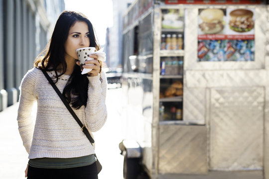 Young woman drinking coffee from disposable glass with concession stand in background