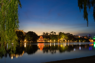 Fototapeta na wymiar Hoan Kiem lake ( Ho Guom, Sword lake), the center of Hanoi capital, Vietnam at twilight. Willow branches on foreground