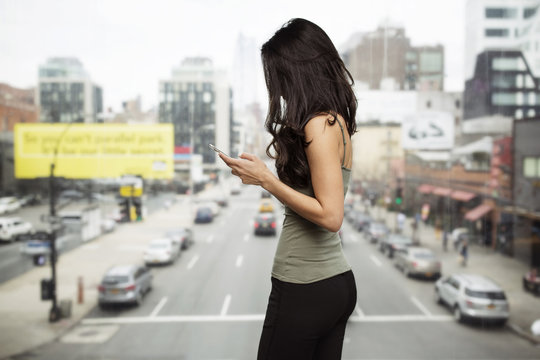 Side view of woman using smart phone by glass window with city street in background
