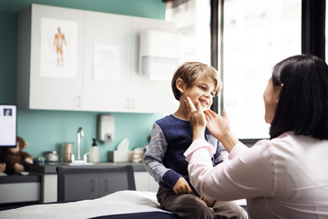 Female doctor examining boy's glands in clinic
