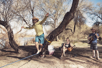 Happy friends holding guitars while watching man slacklining in forest
