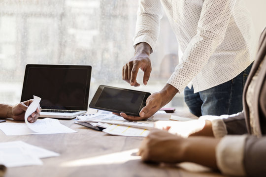 Midsection of businessman showing phablet to colleagues in meeting