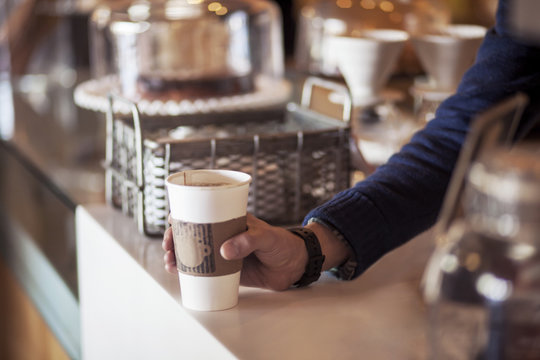 Cropped image of barista holding disposable cup at counter in cafe