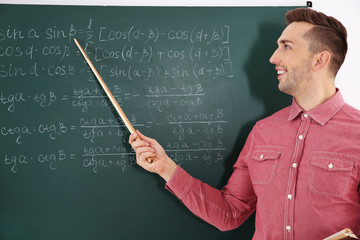 Young male teacher beside blackboard in classroom