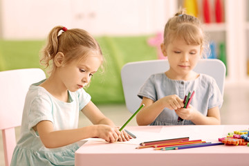 Adorable little sisters drawing and sitting at table