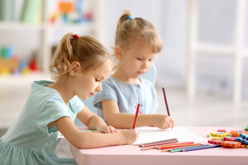 Fototapeta premium Adorable little sisters drawing and sitting at table