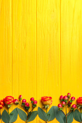 Fototapeta na wymiar Hypericum, roses and rowan on yellow wooden background