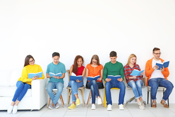 Obraz premium Group of people reading books while sitting near light wall