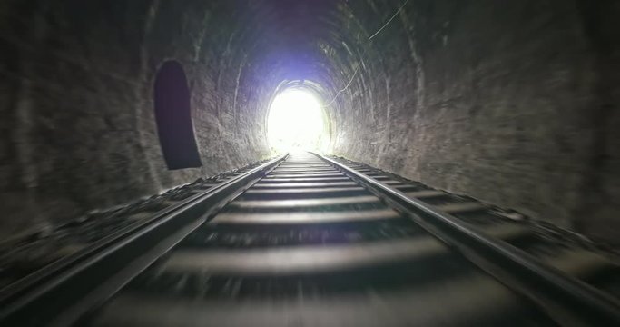 Fast moving camera in dark old railway tunnel toward bright light in the end