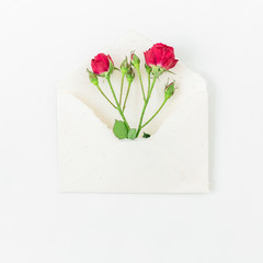 Red roses and envelope on white background. Flat lay, Top view.