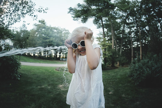 Water splashing over scared girl wearing sunglasses at backyard