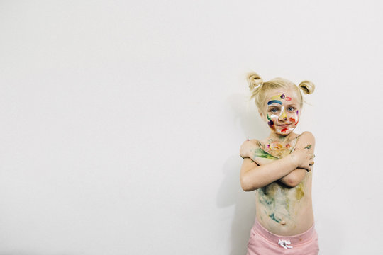 Cute Girl Covered In Messy Paint Standing Against White Wall