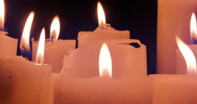 Close up view of many candles burning with warm fire in darkness 4K video background