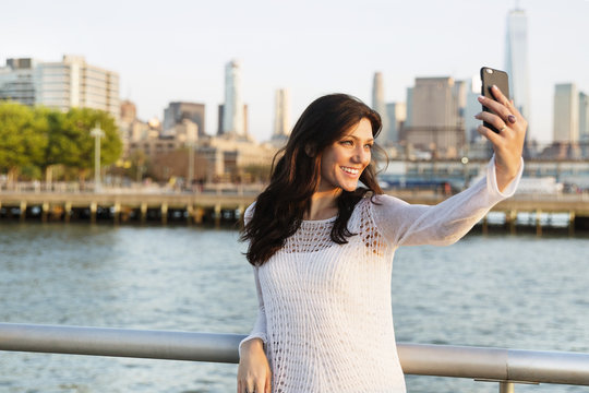 Happy woman taking selfie while standing on promenade with One World Trade Center in background